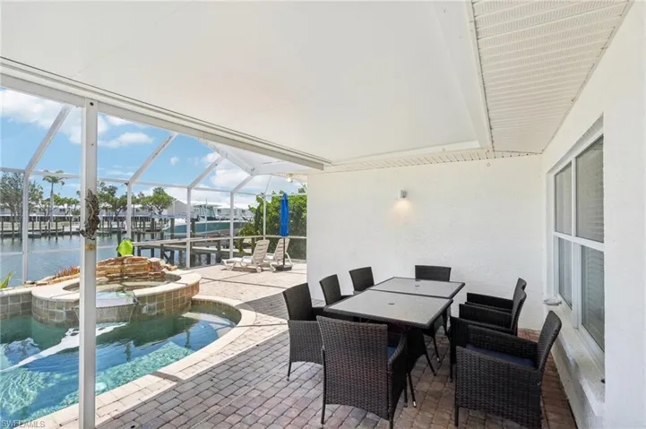 View of patio with a water view, glass enclosure, a pool with connected hot tub, and outdoor dining space