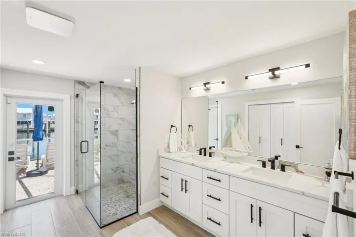 Full bathroom with a stall shower, recessed lighting, double vanity, baseboards, and wood finished floors