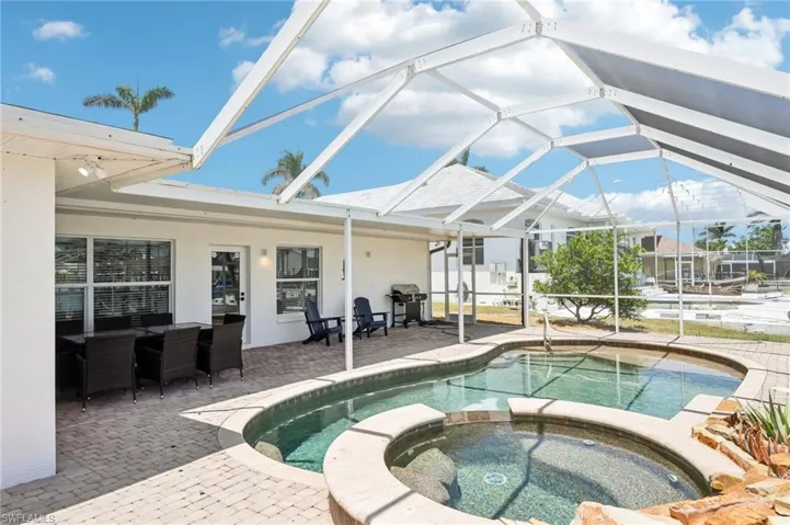 View of pool featuring a patio, a pool with connected hot tub, a grill, and glass enclosure
