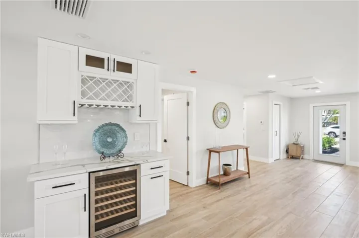 Indoor dry bar with wine cooler, decorative backsplash, baseboards, light wood finished floors, and recessed lighting