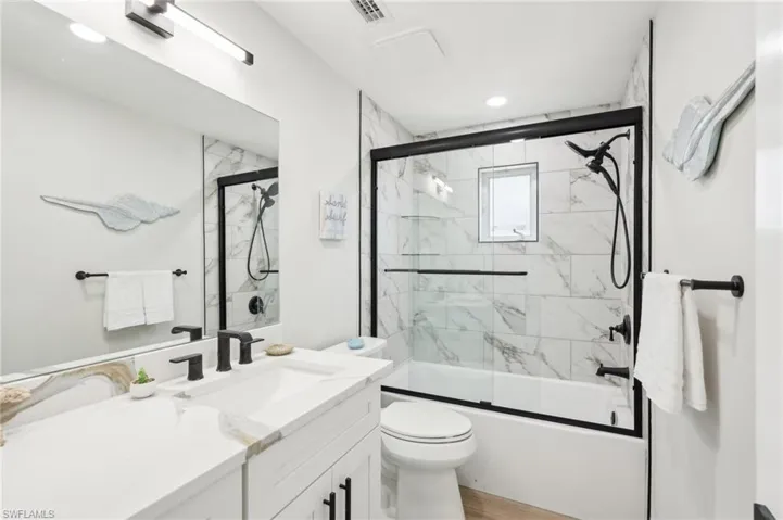 Bathroom featuring combined bath / shower with glass door, vanity, toilet, and recessed lighting