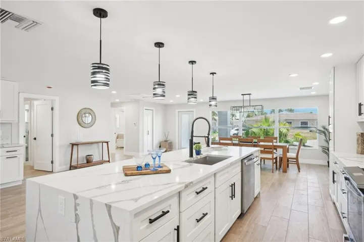 Kitchen with a sink, an island with sink, recessed lighting, white cabinets, and light wood-style flooring