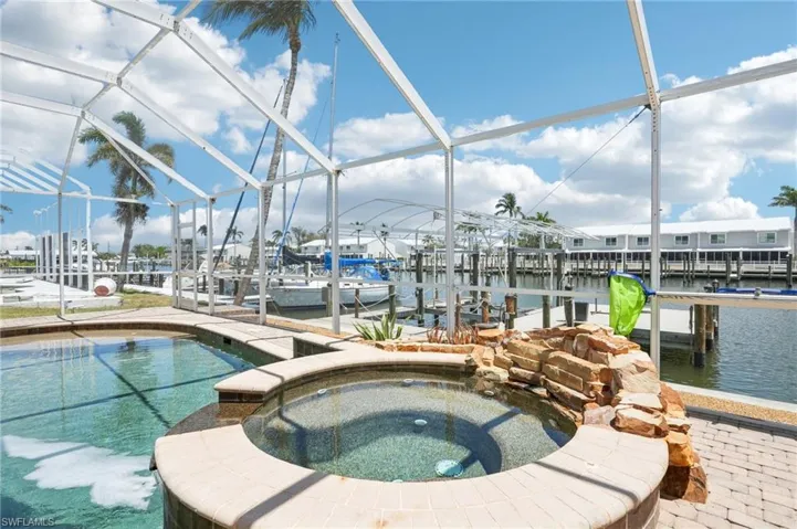 View of pool with boat lift, a dock, a lanai, a water view, and a pool with connected hot tub