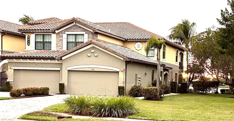 Mediterranean / spanish-style home with stucco siding, driveway, stone siding, a front lawn, and a tiled roof