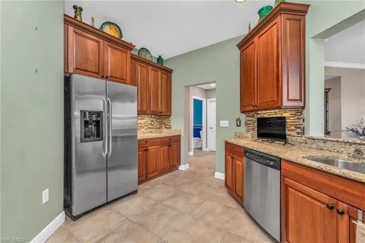 Kitchen with stainless steel appliances, light stone counters, decorative backsplash, wood finish cabinetry, and light tile patterned floors
