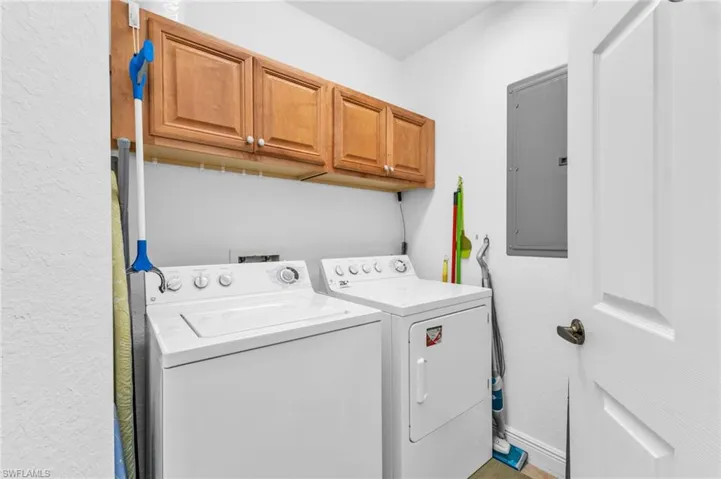 Laundry area with electric panel, washing machine and clothes dryer, cabinet space, and a textured wall
