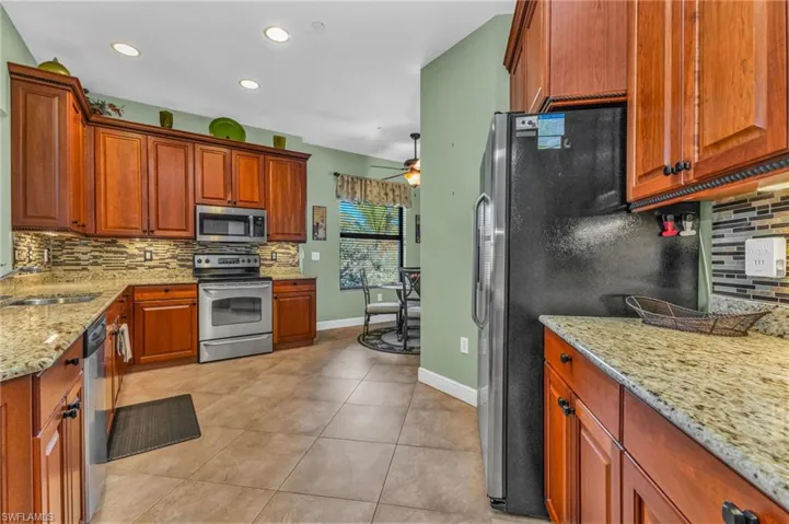 Kitchen featuring decorative backsplash, stainless steel appliances, light stone counters, light tile patterned floors, and wood finish cabinets