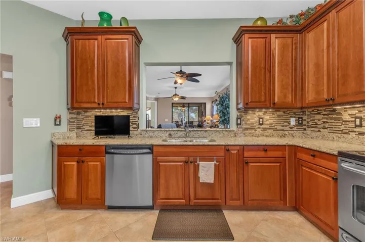 Kitchen with stainless steel appliances, light stone counters, backsplash, and wood finish cabinets