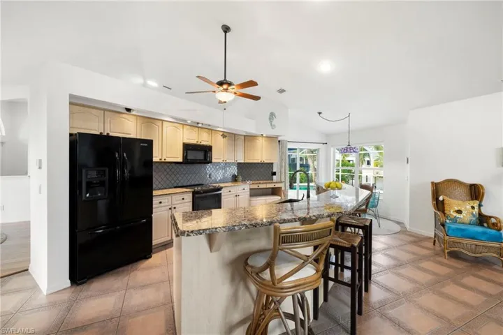 Kitchen featuring black appliances, decorative backsplash, a breakfast bar, dark stone countertops, and a kitchen island with sink