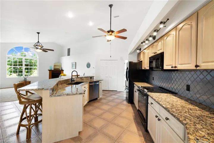 Kitchen with black appliances, dark stone countertops, decorative backsplash, a breakfast bar, and a spacious island
