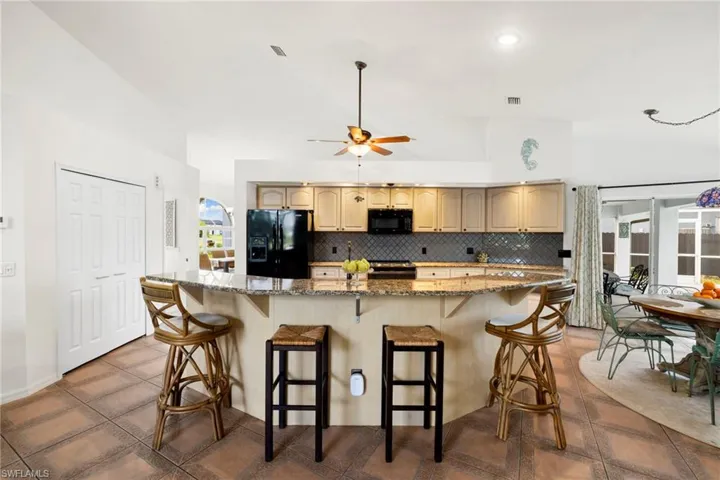 Kitchen with a spacious island, decorative backsplash, black appliances, light stone counters, and a kitchen bar