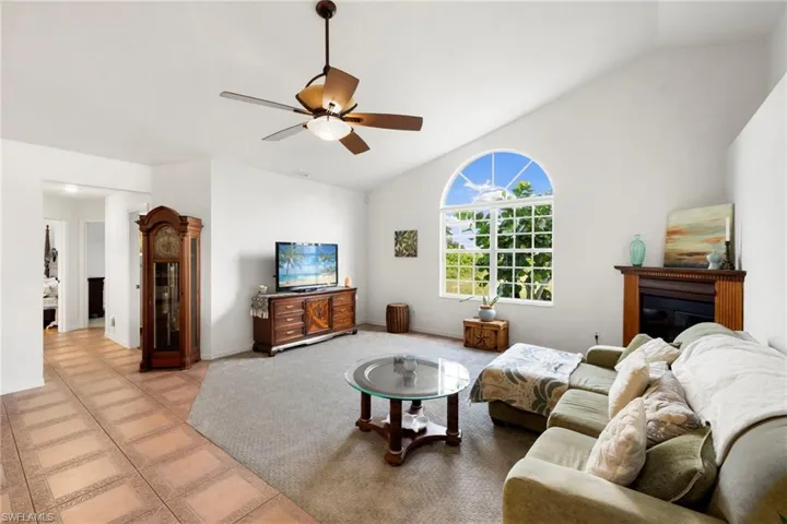 Tiled living area featuring vaulted ceiling, a ceiling fan, and a glass covered fireplace
