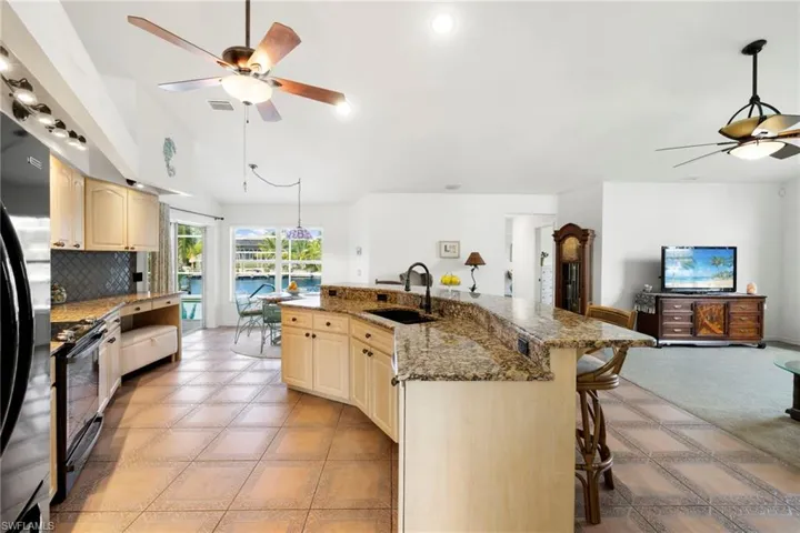 Kitchen featuring ceiling fan, open floor plan, a breakfast bar, a kitchen island with sink, and stainless steel refrigerator