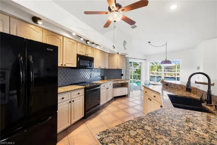 Kitchen with black appliances, backsplash, dark stone countertops, light tile patterned floors, and pendant lighting