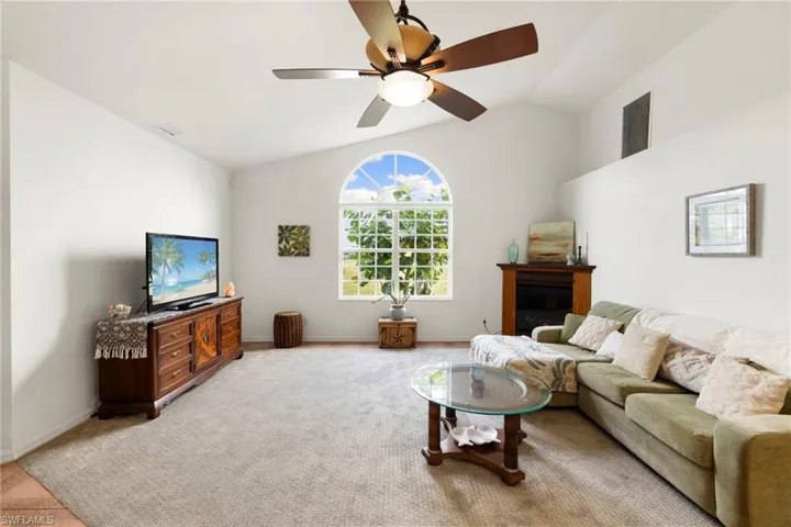 Living room with lofted ceiling, carpet flooring, a glass covered fireplace, and a ceiling fan