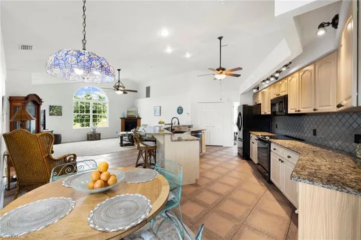 Kitchen with backsplash, black appliances, dark stone counters, open floor plan, and decorative light fixtures