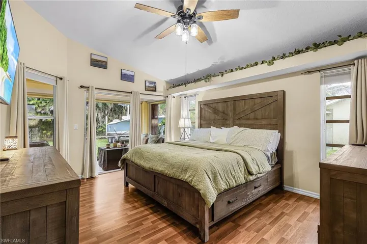 Bedroom featuring access to outside, vaulted ceiling, wood finished floors, and an ensuite bathroom.