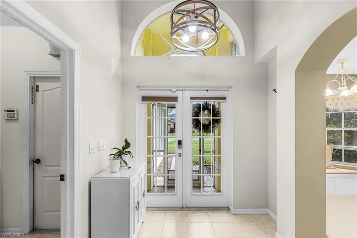 Foyer entrance featuring a chandelier, french doors, light tile patterned floors, arched walkways, and a towering ceiling