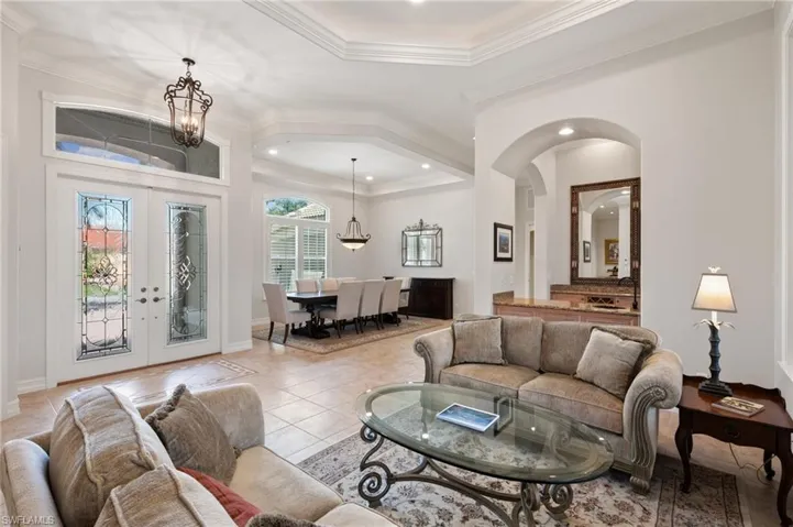 Living room featuring an inviting chandelier, ornamental molding, light tile patterned floors, and french doors
