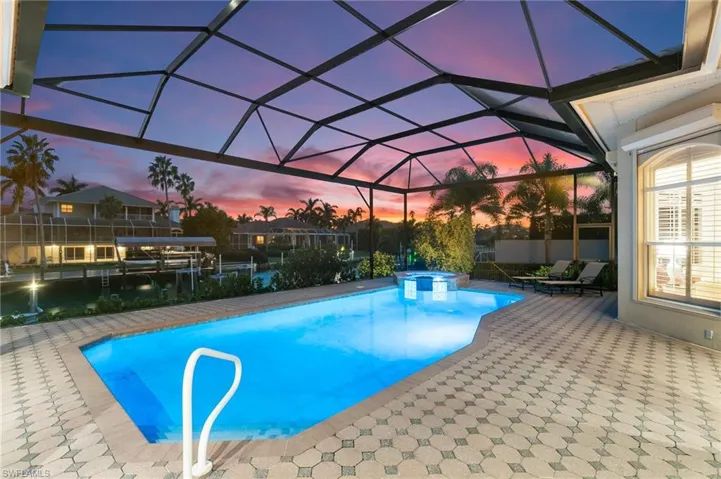 Pool at dusk with glass enclosure and a patio area