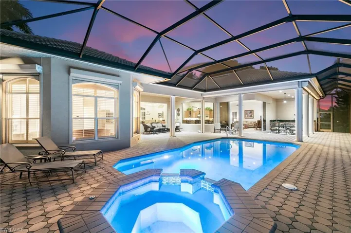 Pool at dusk with glass enclosure, an in ground hot tub, and a patio area