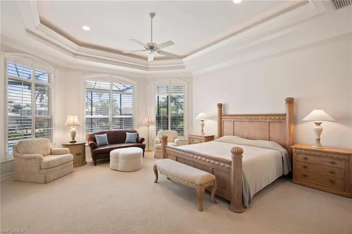Bedroom with ceiling fan, a tray ceiling, and light carpet