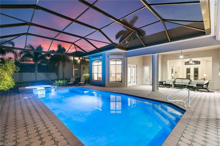 Pool at dusk featuring a lanai, ceiling fan, an in ground hot tub, and a patio area