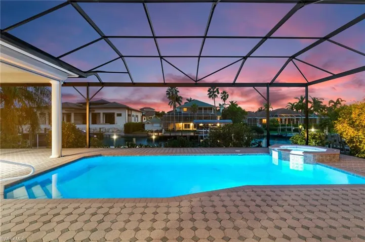 Pool at dusk featuring glass enclosure, an in ground hot tub, and a patio area