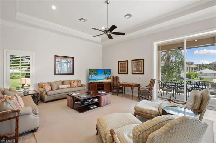 Tiled living room with ornamental molding, a wealth of natural light, ceiling fan, and a raised ceiling