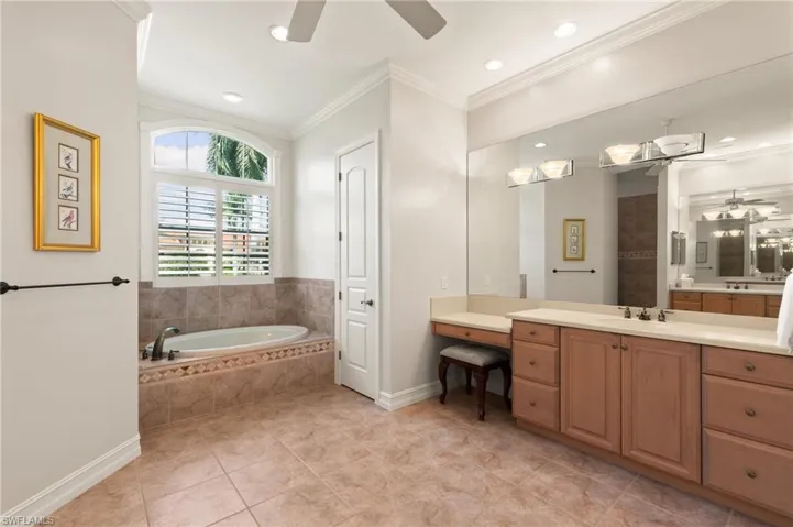 Bathroom featuring crown molding, a relaxing tiled tub, tile patterned floors, ceiling fan, and vanity