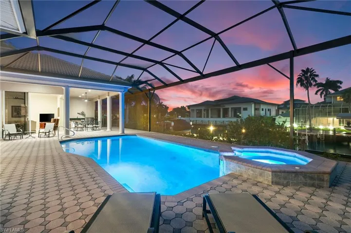 Pool at dusk featuring a lanai, a patio, ceiling fan, and an in ground hot tub