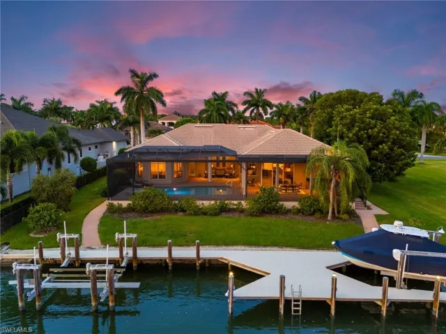 Back house at dusk featuring a water view, glass enclosure, and a yard