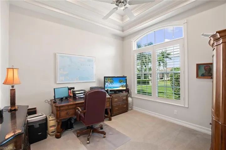 Carpeted office space featuring crown molding, ceiling fan, and a raised ceiling