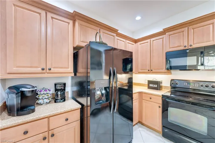 Kitchen with black appliances, light brown cabinetry, and light tile patterned flooring