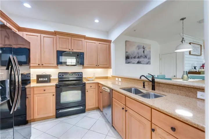 Kitchen featuring light stone counters, sink, black appliances, light tile patterned floors, and decorative light fixtures