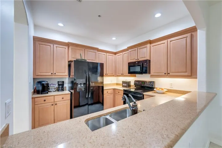Kitchen, light brown cabinets, light stone countertops, black appliances, and sink