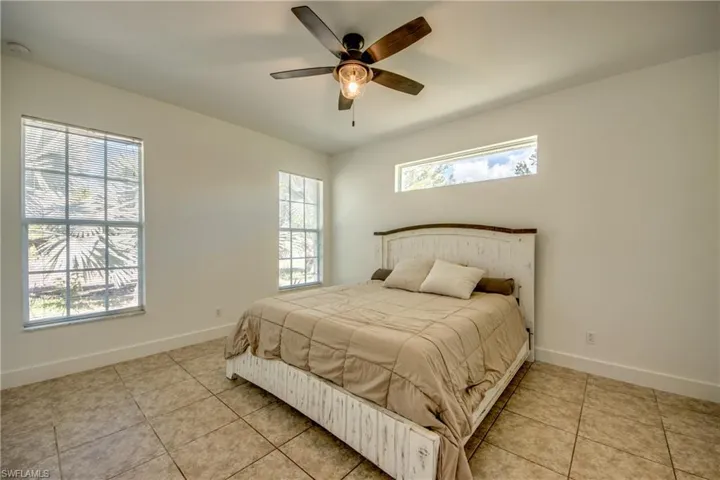 Tiled bedroom with ceiling fan and multiple windows