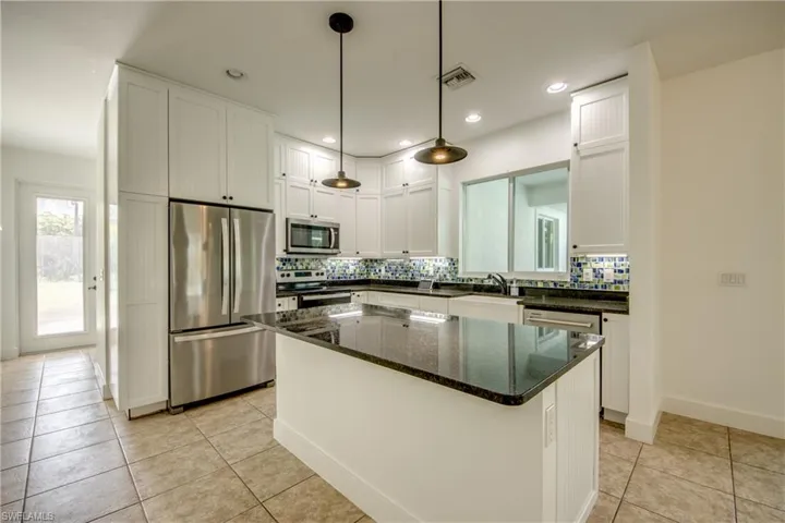 Kitchen with dark granite stone island, stainless steel appliances, and white cabinets