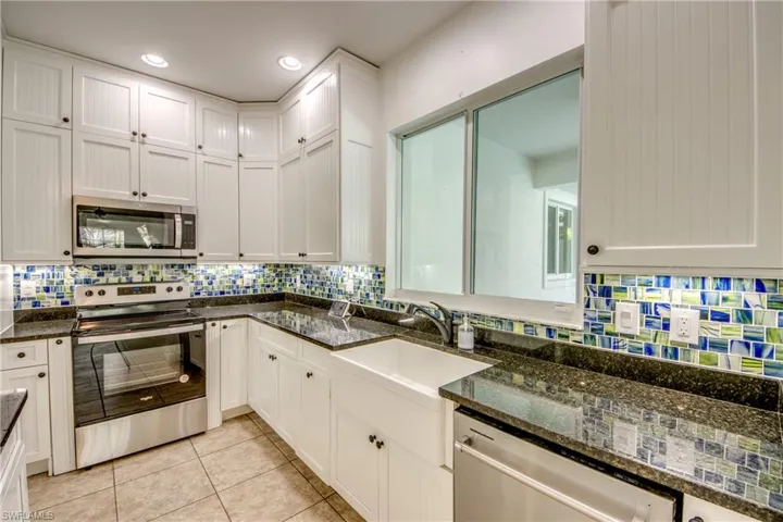 Kitchen with stainless steel appliances, backsplash, white cabinetry, and dark granite stone countertops