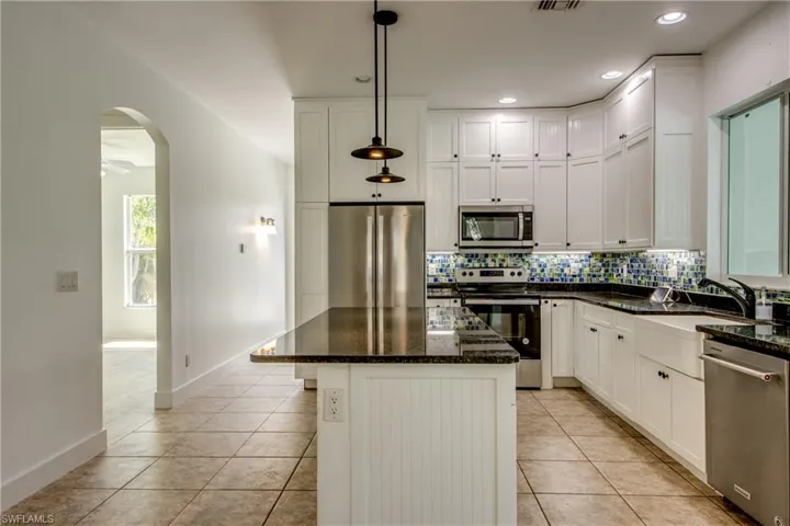 Kitchen featuring stainless steel appliances, backsplash, a center island, light tile floors, and pendant lighting