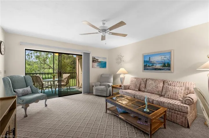 Living area with patterned carpet, a ceiling fan, and sliding glass doors opening to a screened balcony
