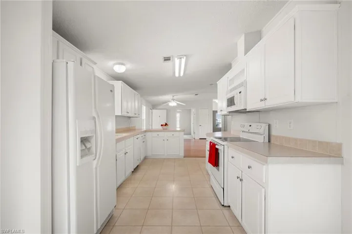 Kitchen featuring white appliances, light countertops, a peninsula, white cabinets, and ceiling fan