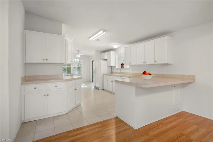 Kitchen featuring a peninsula, white cabinetry, light countertops, a ceiling fan, and white refrigerator with ice dispenser