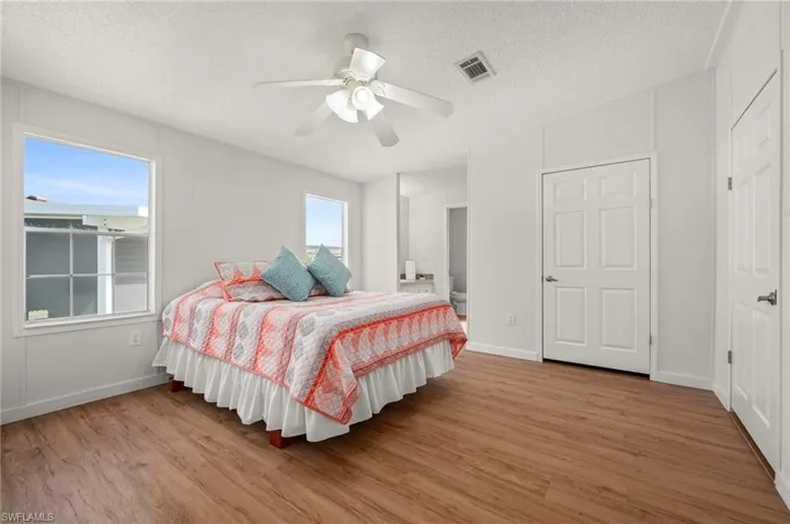 Bedroom featuring light wood finished floors, ensuite bath, a textured ceiling, and ceiling fan