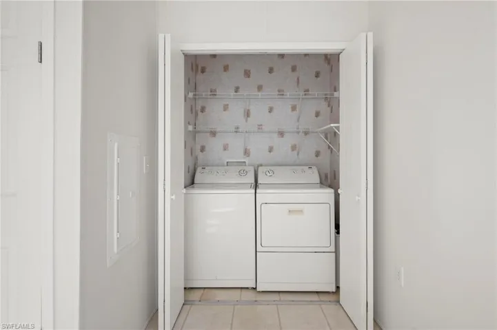 Laundry room featuring electric panel, light tile patterned floors, and independent washer and dryer