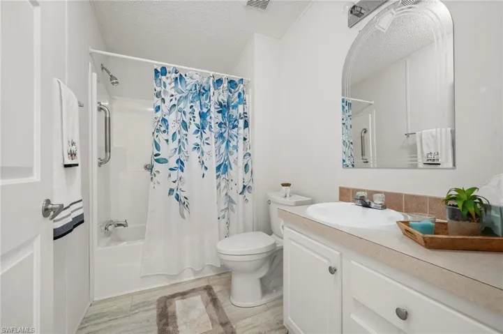 Full bath featuring a textured ceiling, shower / bath combination with curtain, and vanity