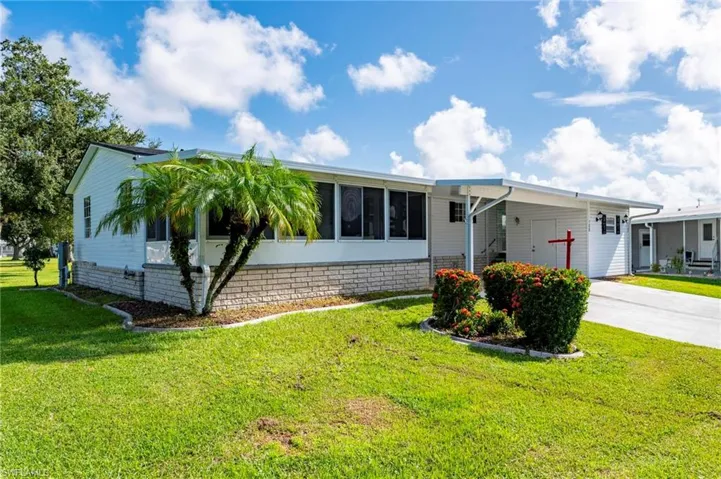 View of front of house with a carport, concrete driveway, a front yard, and a sunroom