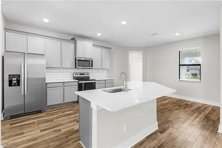 Kitchen featuring stainless steel appliances, gray cabinets, light stone countertops, recessed lighting, and backsplash