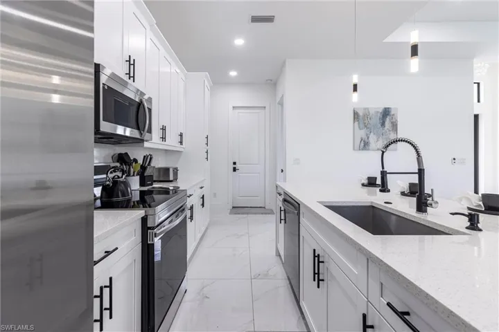 Kitchen with appliances with stainless steel finishes, light quartz countertops, hanging light fixtures, white cabinets, and recessed lighting