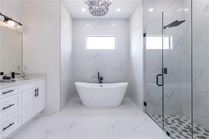 Bathroom with quartz vanities, a marble finish shower, light marble finish flooring, a freestanding tub, and tile walls